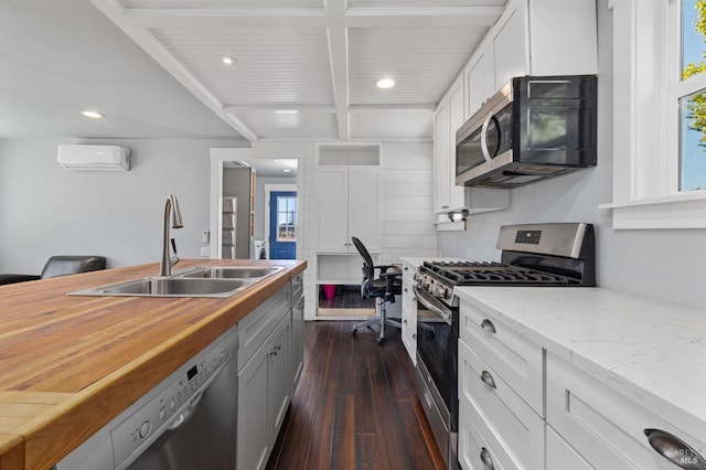 kitchen with a sink, a wall unit AC, stainless steel appliances, white cabinets, and dark wood-type flooring