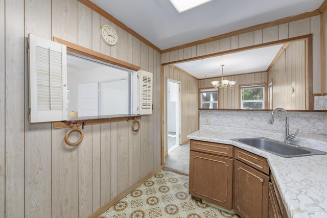 kitchen featuring wood walls, sink, decorative backsplash, hanging light fixtures, and an inviting chandelier