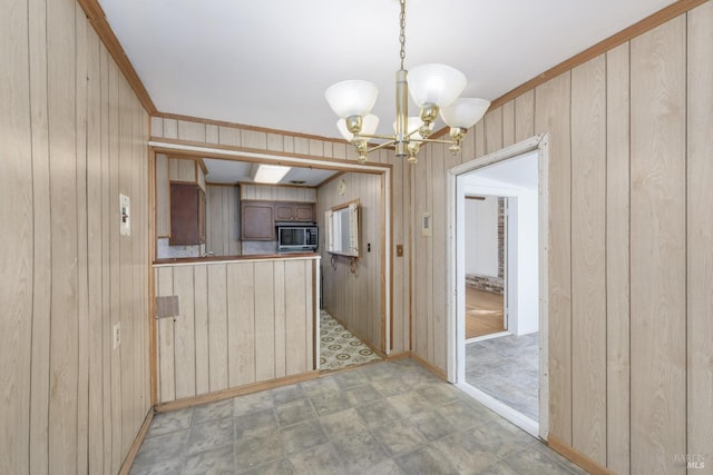 kitchen featuring pendant lighting, ornamental molding, a chandelier, and wood walls