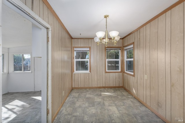 unfurnished dining area with a notable chandelier, crown molding, and wood walls