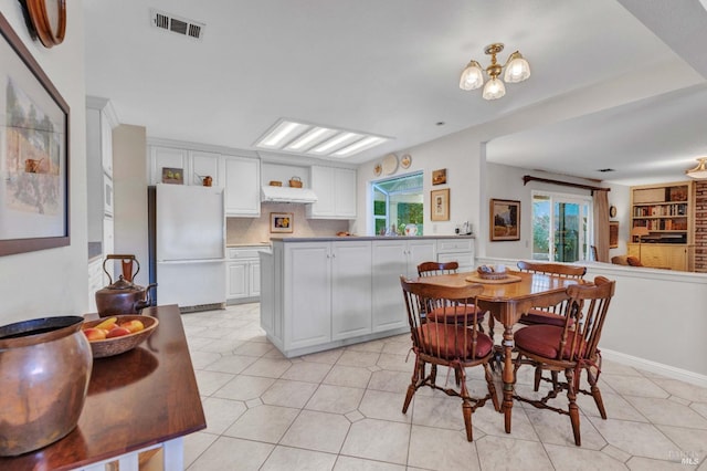 kitchen with backsplash, white cabinetry, white fridge, light tile patterned floors, and a chandelier