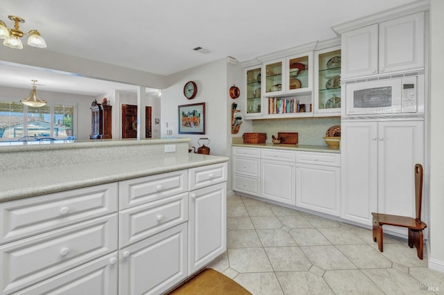 kitchen featuring white cabinetry, white microwave, light tile patterned flooring, and decorative light fixtures