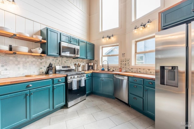 kitchen featuring light tile patterned floors, stainless steel appliances, wooden counters, sink, and a towering ceiling