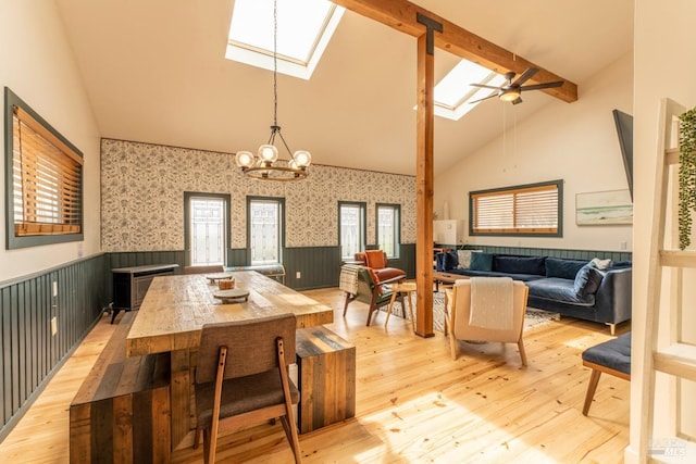 dining area with a skylight, a healthy amount of sunlight, light hardwood / wood-style flooring, ceiling fan with notable chandelier, and high vaulted ceiling