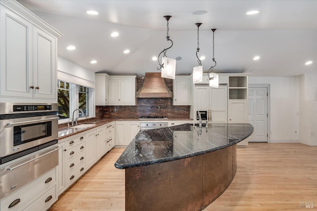 kitchen featuring custom exhaust hood, oven, sink, pendant lighting, and an island with sink