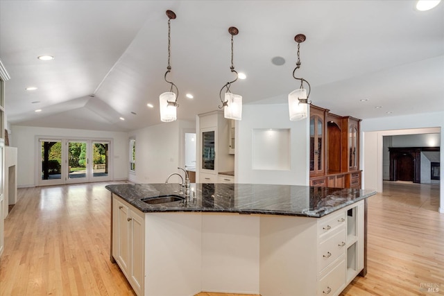 kitchen with pendant lighting, lofted ceiling, dark stone countertops, sink, and a kitchen island with sink