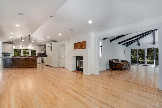 unfurnished living room with sink, lofted ceiling with beams, and light hardwood / wood-style flooring