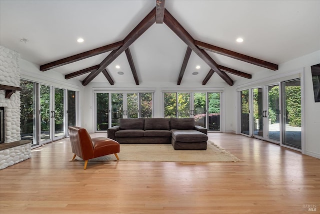 living room with light hardwood / wood-style flooring, a stone fireplace, and vaulted ceiling with beams