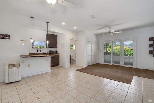 kitchen with dark brown cabinetry, hanging light fixtures, ceiling fan, a breakfast bar, and light tile patterned floors