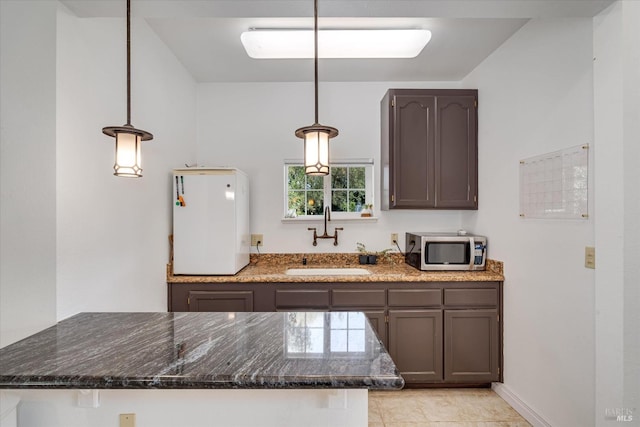 kitchen featuring dark brown cabinetry, decorative light fixtures, dark stone counters, sink, and light tile patterned floors