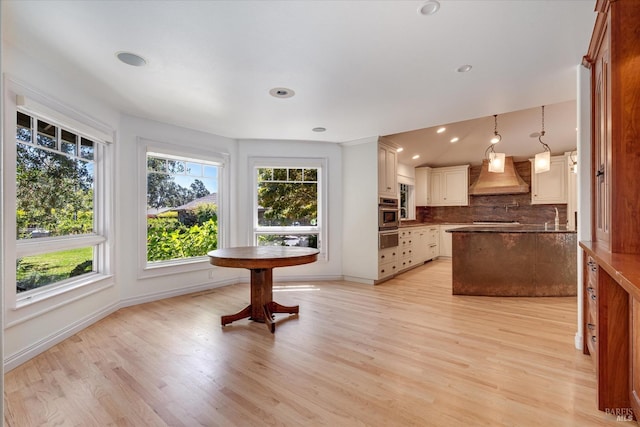 kitchen with custom exhaust hood, light hardwood / wood-style floors, decorative backsplash, and hanging light fixtures