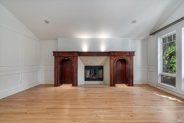 unfurnished living room with vaulted ceiling, a high end fireplace, and light hardwood / wood-style floors