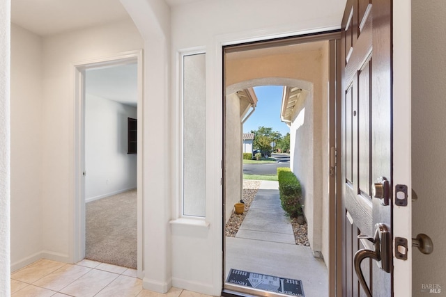 foyer entrance featuring arched walkways, light carpet, baseboards, and light tile patterned floors