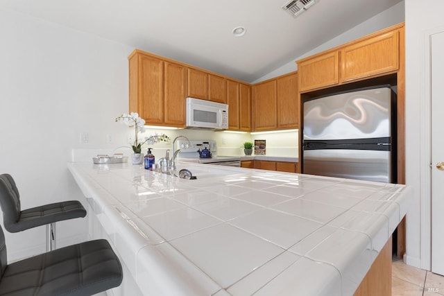 kitchen featuring white microwave, range with electric cooktop, visible vents, tile counters, and freestanding refrigerator