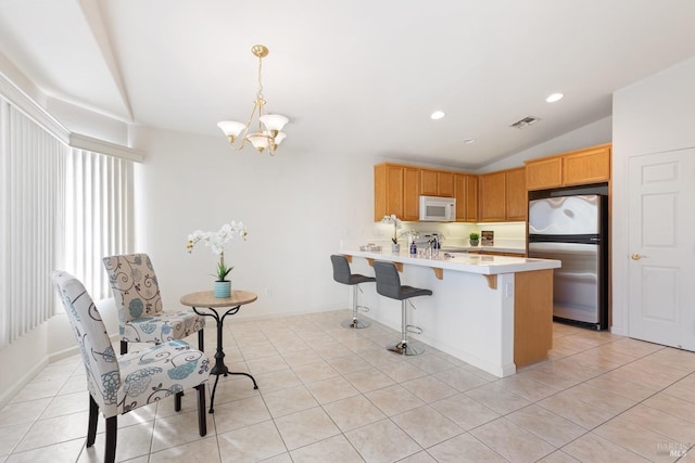 kitchen with light tile patterned floors, white microwave, freestanding refrigerator, a peninsula, and light countertops