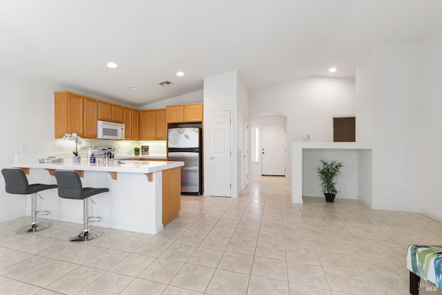 kitchen with visible vents, white microwave, freestanding refrigerator, a peninsula, and light countertops