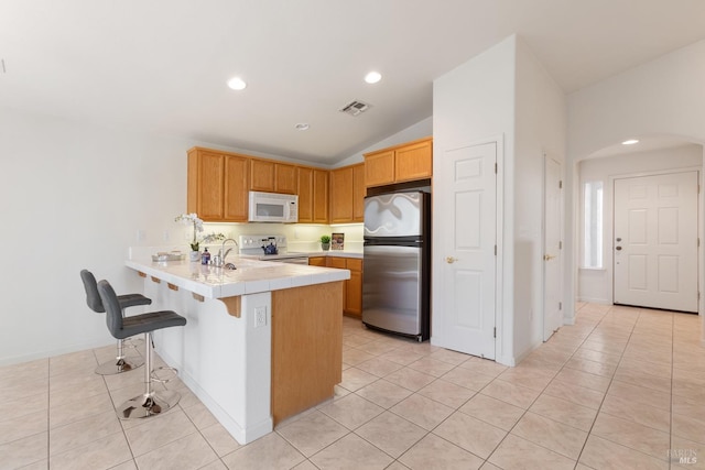 kitchen with arched walkways, light tile patterned flooring, a peninsula, white appliances, and visible vents