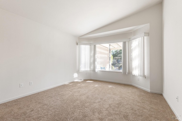 carpeted spare room featuring lofted ceiling and baseboards