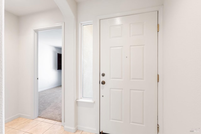 entrance foyer with baseboards, arched walkways, light colored carpet, and light tile patterned flooring