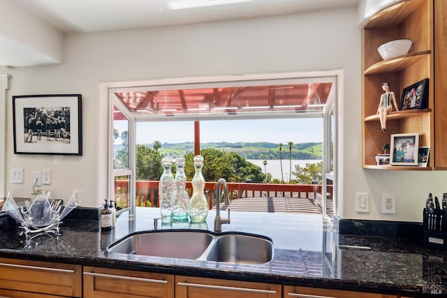 kitchen featuring dark stone countertops, sink, and a water view