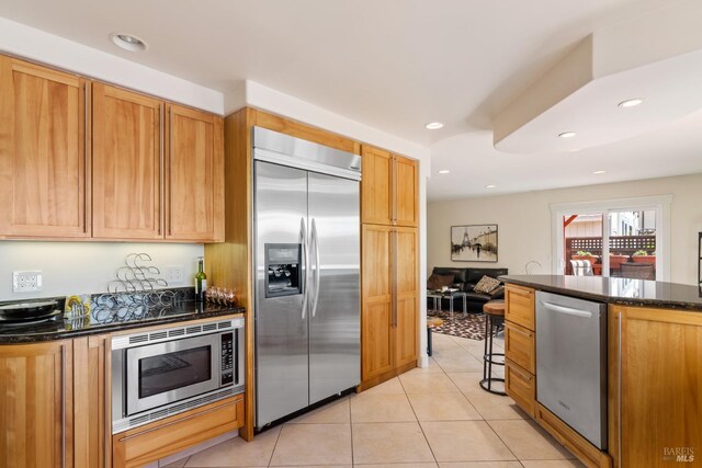 kitchen with built in appliances, dark stone counters, and light tile patterned flooring