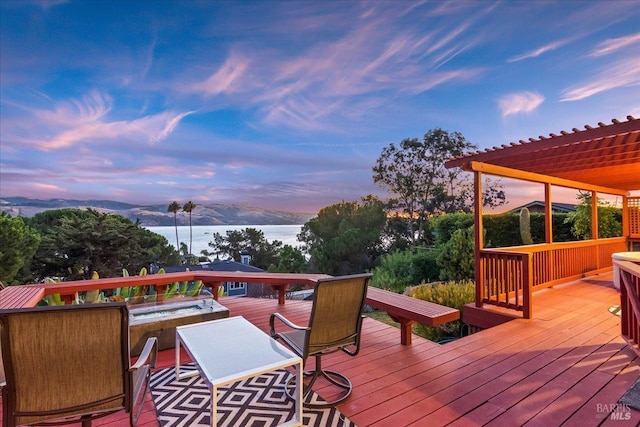 deck at dusk featuring a water and mountain view and a pergola