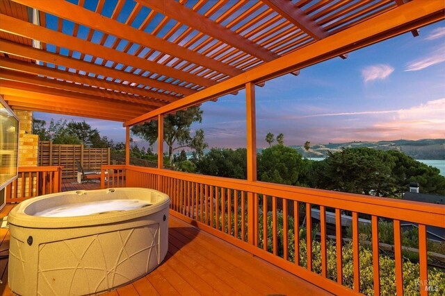 deck at dusk with a hot tub and a pergola