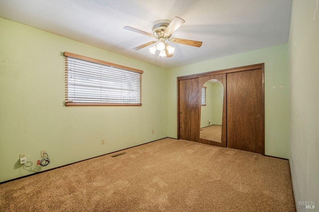 unfurnished bedroom with a textured ceiling, ceiling fan, a closet, and carpet floors