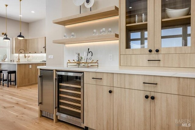 bar featuring beverage cooler, decorative light fixtures, light brown cabinets, and light hardwood / wood-style floors