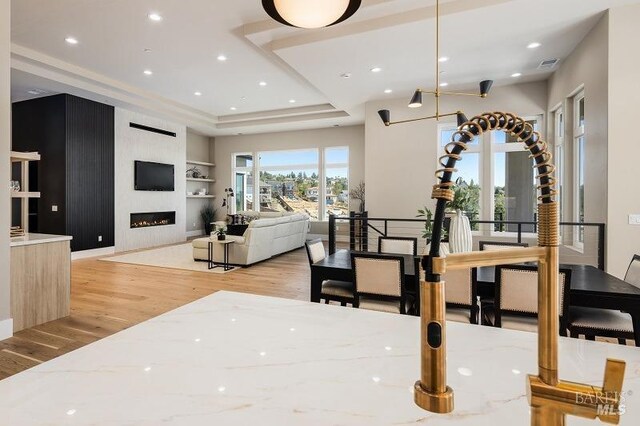 kitchen with a tray ceiling, light hardwood / wood-style flooring, light stone counters, and hanging light fixtures