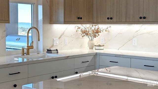 kitchen with backsplash, light stone countertops, and sink