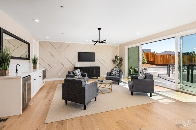 living room with light hardwood / wood-style flooring, wine cooler, sink, and wooden walls