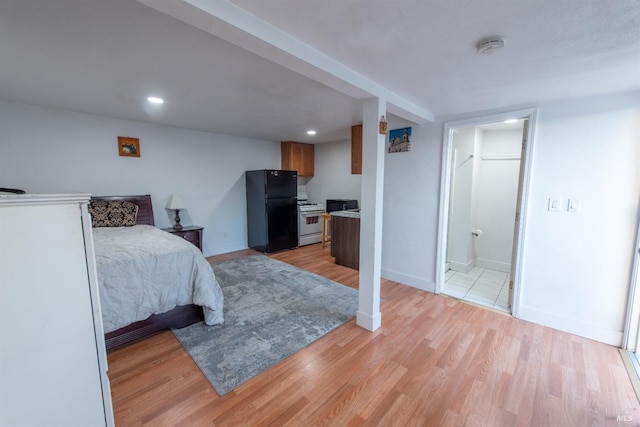 bedroom with connected bathroom, light hardwood / wood-style flooring, and black refrigerator