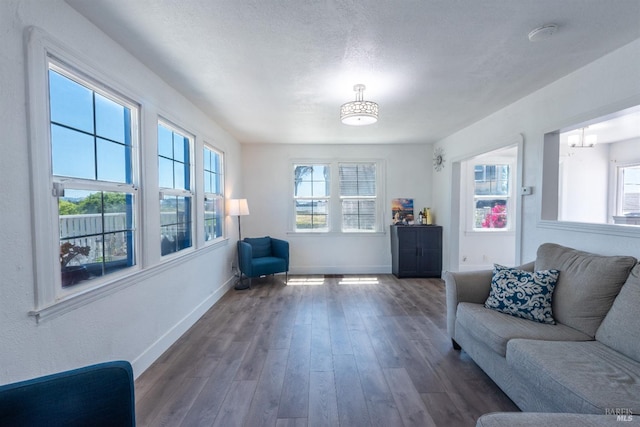 living room with dark wood-type flooring, a notable chandelier, a textured ceiling, and a healthy amount of sunlight