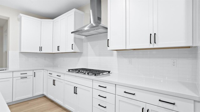 kitchen featuring backsplash, wall chimney range hood, light hardwood / wood-style flooring, white cabinets, and stainless steel gas stovetop