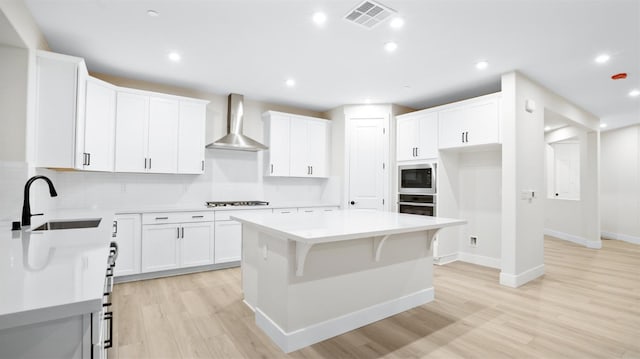 kitchen with built in microwave, wall chimney exhaust hood, a center island, sink, and white cabinetry