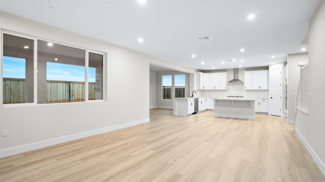 kitchen with a center island, white cabinets, sink, wall chimney exhaust hood, and light wood-type flooring