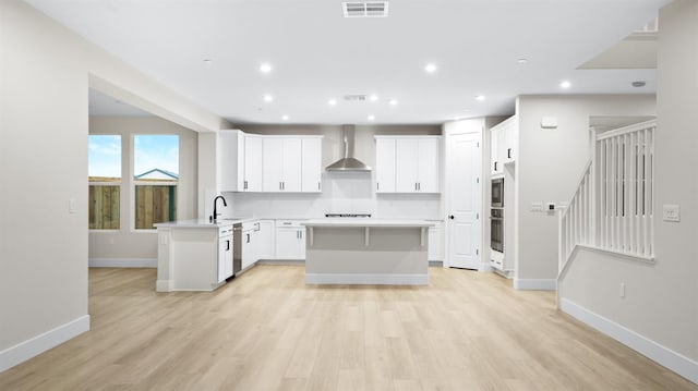 kitchen with light hardwood / wood-style flooring, wall chimney exhaust hood, sink, white cabinetry, and kitchen peninsula