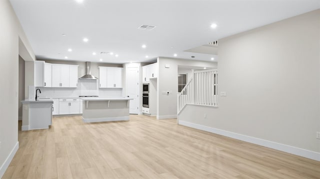 kitchen with a center island, white cabinets, wall chimney range hood, light hardwood / wood-style floors, and stovetop