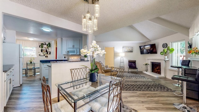 dining room featuring light wood-type flooring, vaulted ceiling, a textured ceiling, and a chandelier