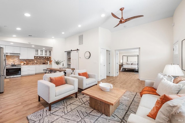 living room with a towering ceiling, a barn door, and light hardwood / wood-style floors