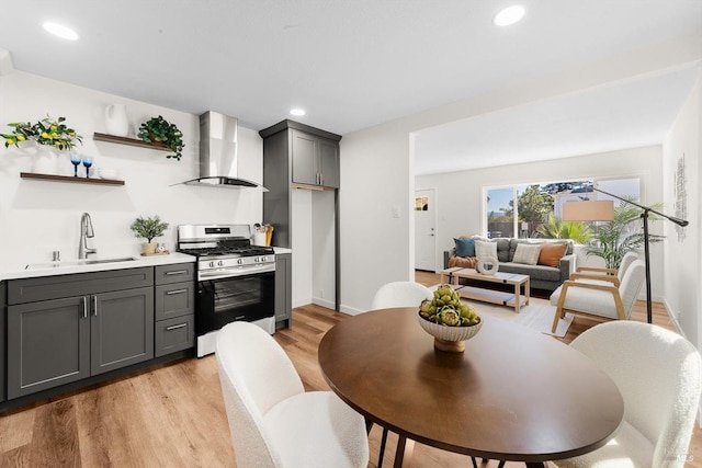 kitchen with sink, gray cabinetry, stainless steel range with gas stovetop, wall chimney exhaust hood, and light wood-type flooring