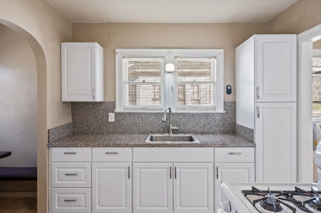 kitchen with sink, white cabinets, gas range oven, and decorative backsplash