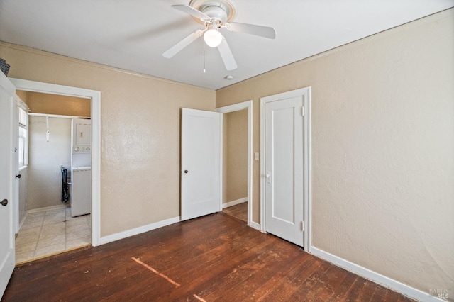 unfurnished bedroom featuring stacked washer / drying machine, dark hardwood / wood-style floors, and ceiling fan