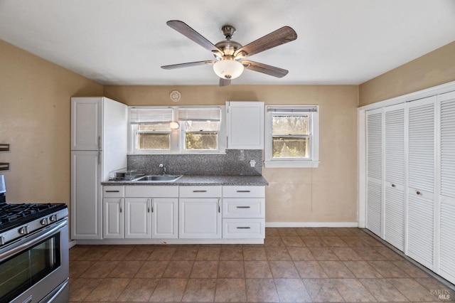 kitchen with stainless steel gas range, sink, white cabinets, ceiling fan, and backsplash