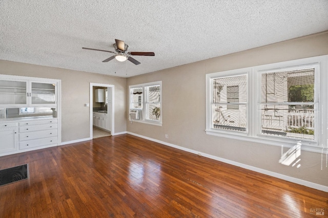 unfurnished bedroom featuring ceiling fan, cooling unit, ensuite bathroom, a textured ceiling, and dark hardwood / wood-style flooring