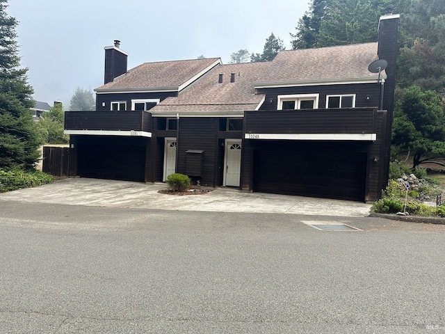 view of front of home with a shingled roof, a chimney, driveway, a balcony, and an attached garage