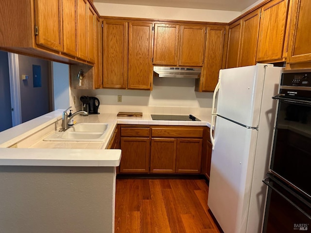 kitchen featuring a peninsula, a sink, black appliances, under cabinet range hood, and brown cabinets