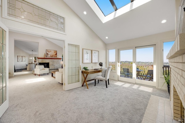 living area featuring a skylight, high vaulted ceiling, light colored carpet, and a brick fireplace