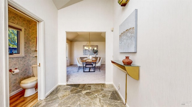 hallway featuring an inviting chandelier, lofted ceiling, and carpet